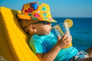 Summer bucket list; Boy kid in armchair with juice glass on beach against sea