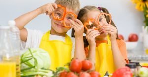 Happy kids having fun with food vegetables at kitchen holds pepper before his eyes like in glasses; blog: How to Encourage Good Nutrition For Kids