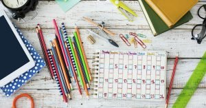 assortment of school supplies laid out on table; blog: 10 Tips for Making A Daily Schedule for Kids When School’s Out