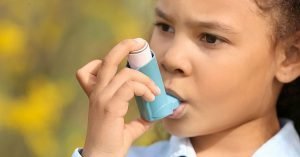 African-American girl with inhaler having asthma attack outdoors on spring day; blog: 6 Tips for Managing Asthma Symptoms in Kids