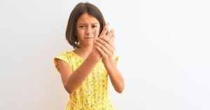 Young beautiful child girl wearing yellow floral dress standing over isolated white background Suffering pain on hands and fingers, arthritis inflammation; blog: What is Juvenile Arthritis?
