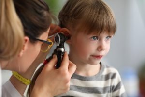 Pediatrician examines ear of sick child in office of hospital background; blog: Ear Nose and Throat Conditions Common in Children