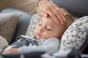 Sick child, toddler boy lying in bed with a fever, resting at home / blog - flu symptoms in children