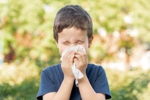 Young boy sneezing outdoors in autumn setting.