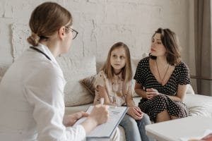 Pediatrician consulting with young girl and mother in clinical office setting.
